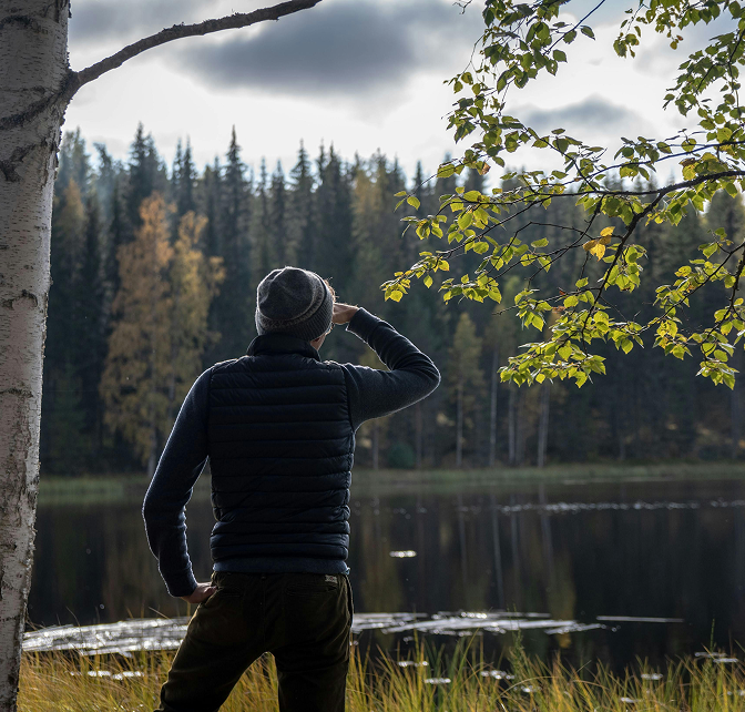 Man with a jacket and hat standing and looking over a pond