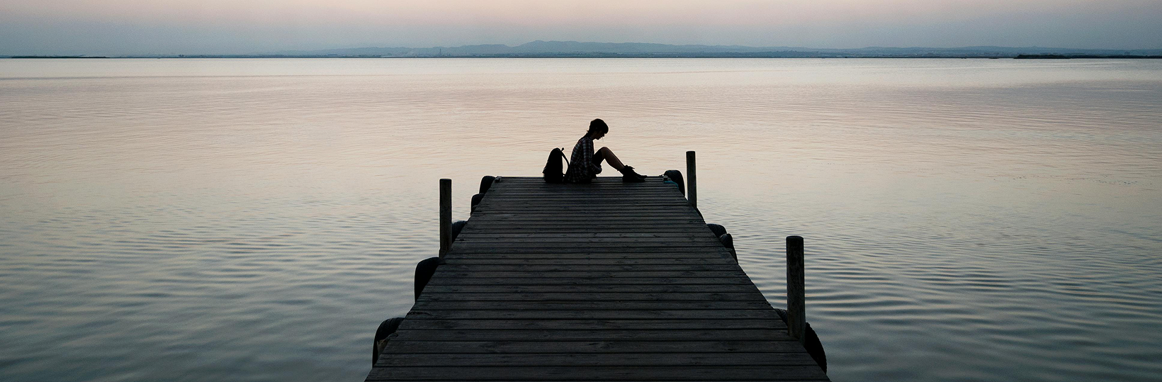 Gloomy photo of a person sitting at the end of a dock